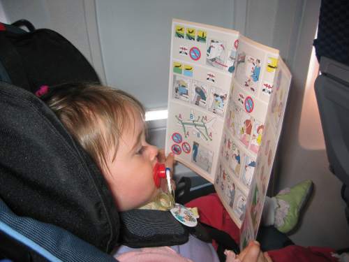 Carolyn, strapped into her seat on the plane, solemnly looks over the airline safety information card.
