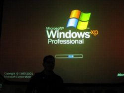Tantek elik stands silhouetted in front of a projection screen on which can be seen a giant Windows XP bootup screen.