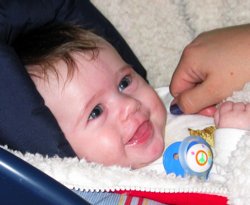 Carolyn, reclining in her car seat while in semi-profile, looks up and to the right with a broad grin on her face.  Kat's hand rests next to Carolyn's left shoulder.