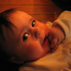 A closeup of Carolyn lying on the floor and look out of the corners of her eyes toward the camera, with her left hand near her chin and the index finger extended into the corner of her mouth.